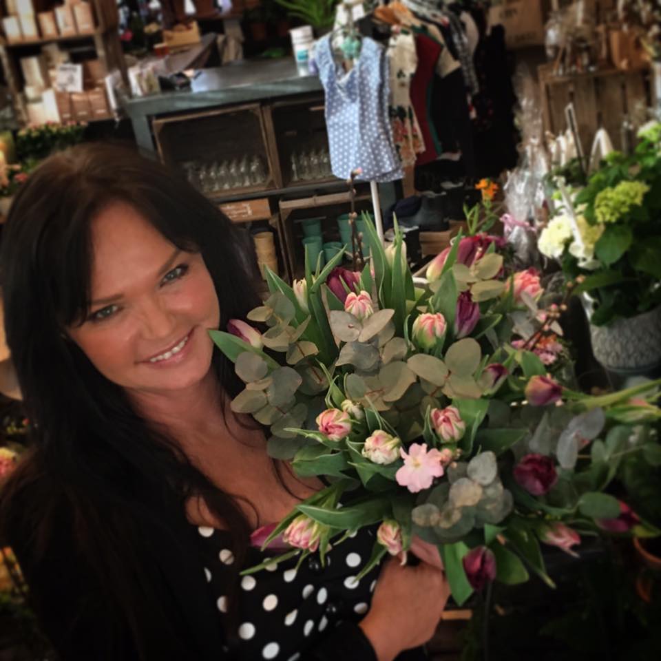 Blomsterdekoratør fra Stokkaveien Blomster holder en bukett med rosa tulipaner og grønne blader.