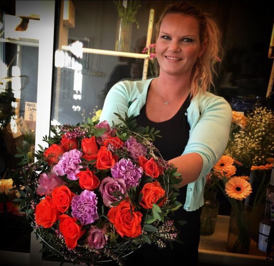 Florist hos Stokkaveien Blomster viser fram en bukett med røde roser og lilla nelliker.